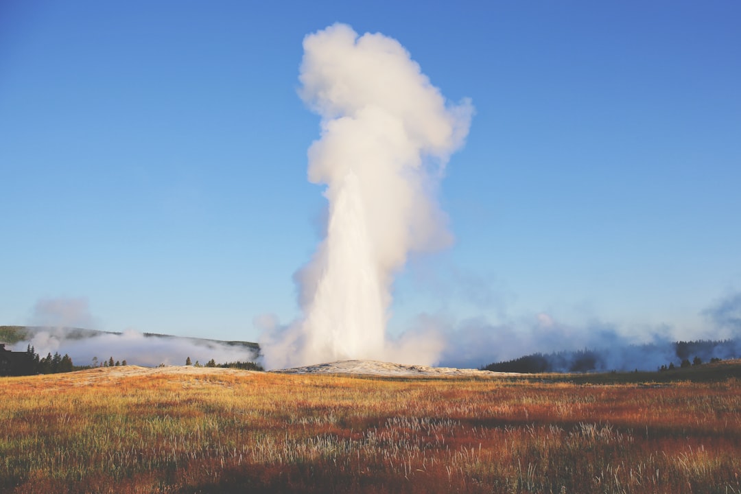 Old Faithful geyser erupting at Yellowstone National Park with a plume of steam against a blue sky